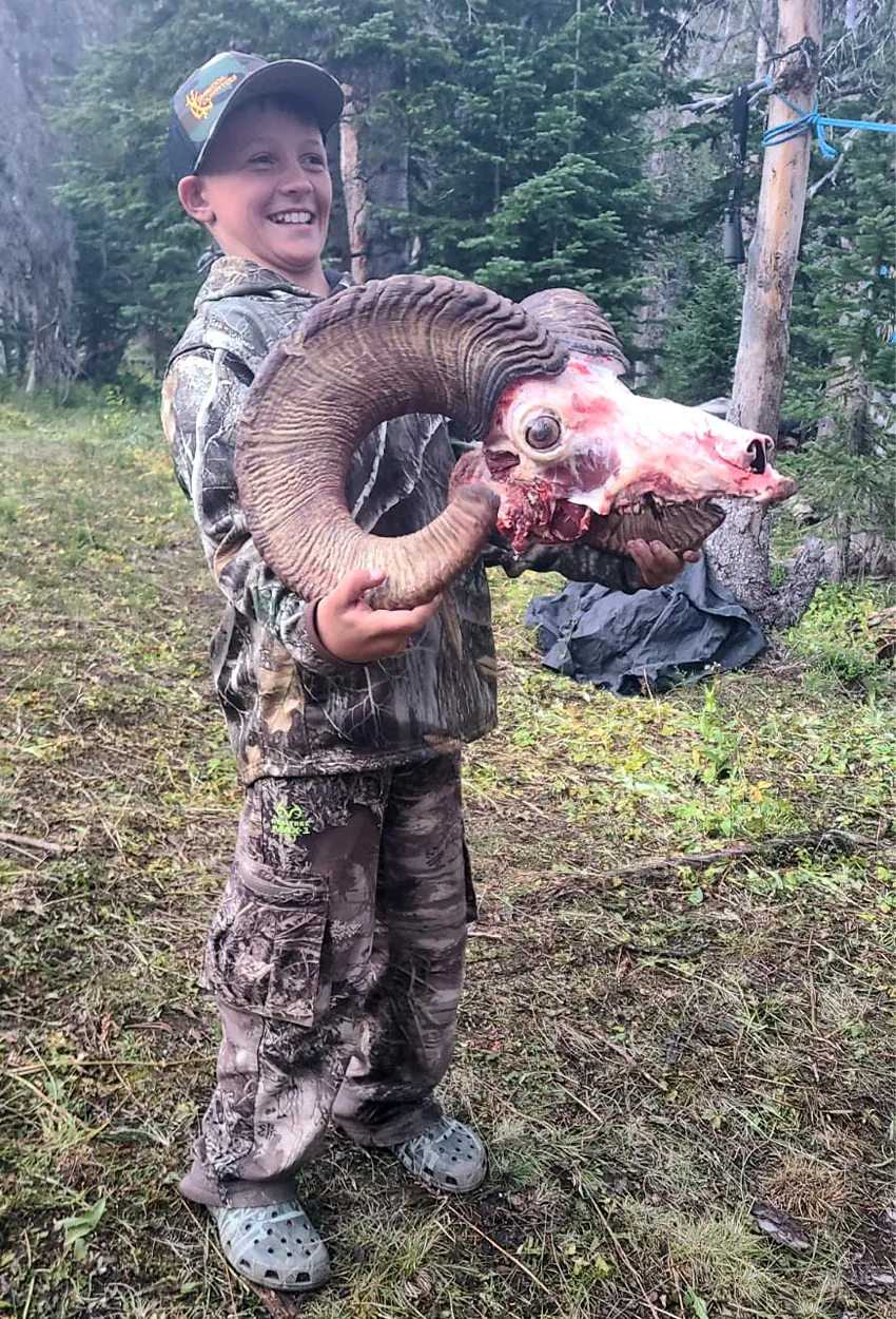 Un jeune chasseur tient un crâne de bélier à grosses cornes.