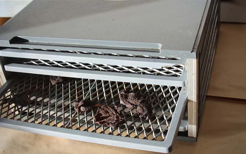 Un déshydrateur de style armoire argentée avec des plateaux contenant de la viande séchée