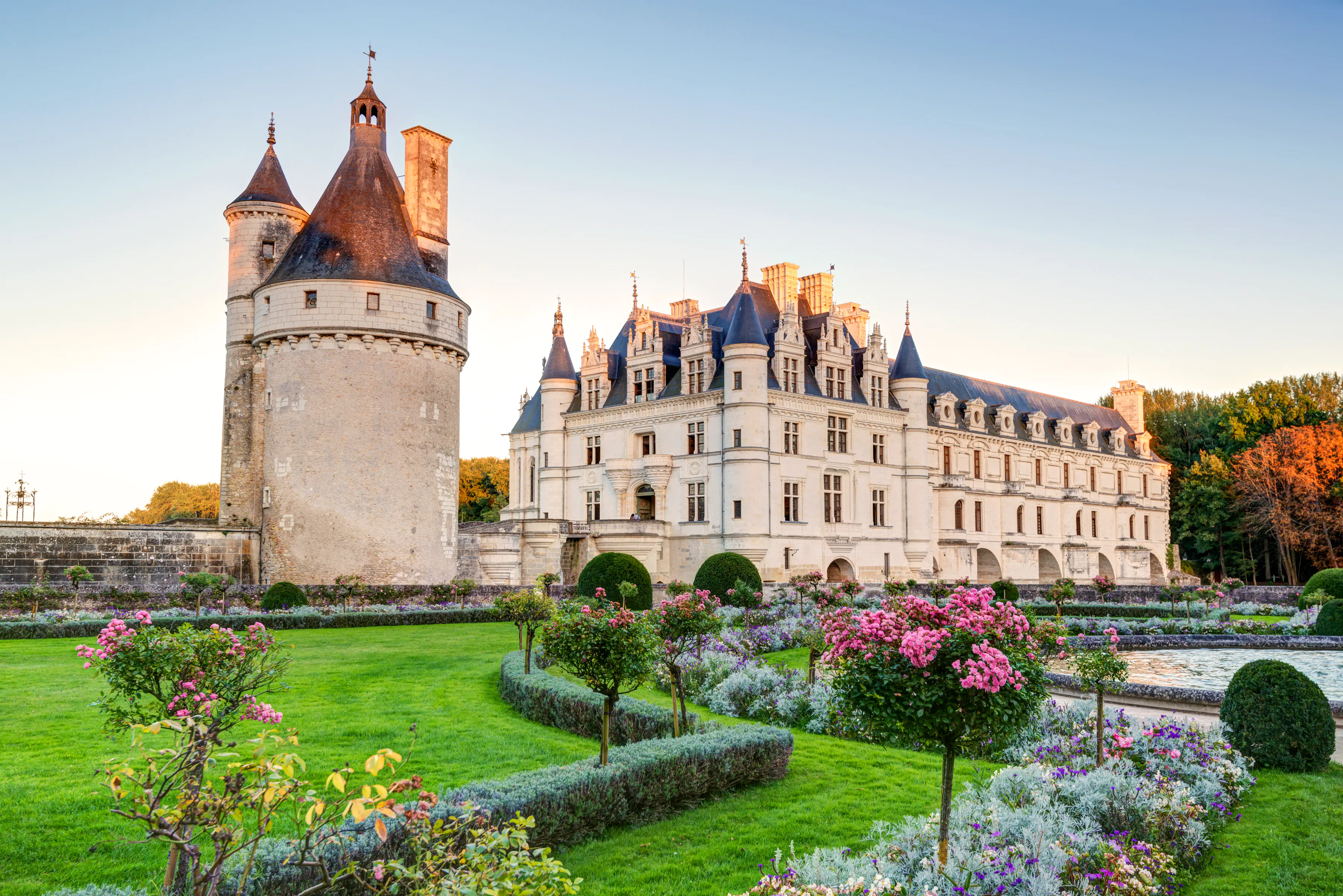 Une photo à travers des jardins à la française vers un château avec une tourelle arrondie
