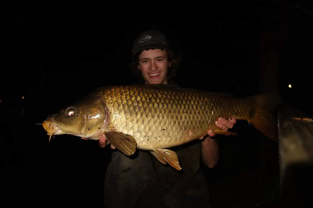 Un pêcheur dans le noir avec une grosse carpe.