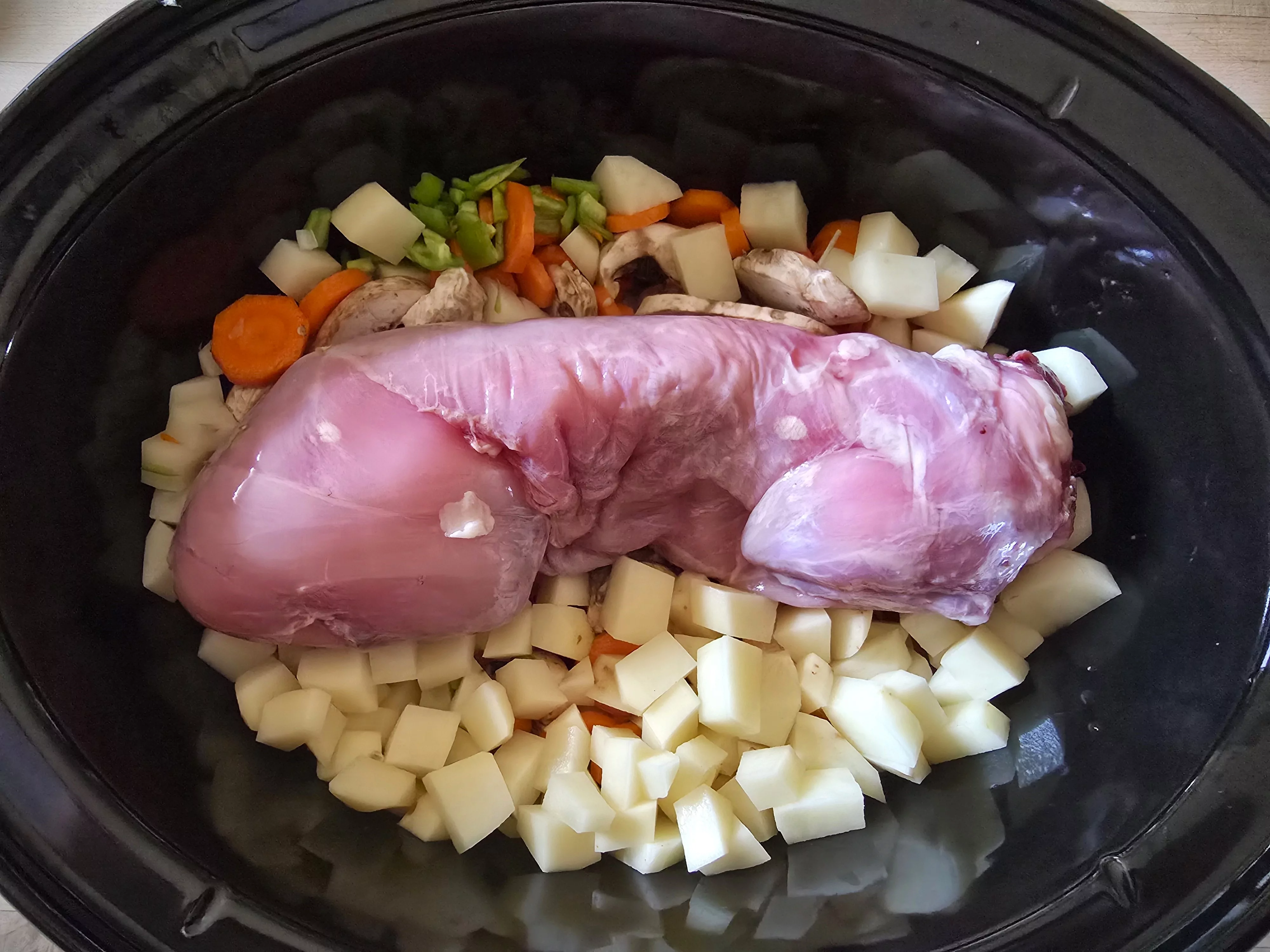 Un lapin écorché dans une mijoteuse entouré de légumes hachés.