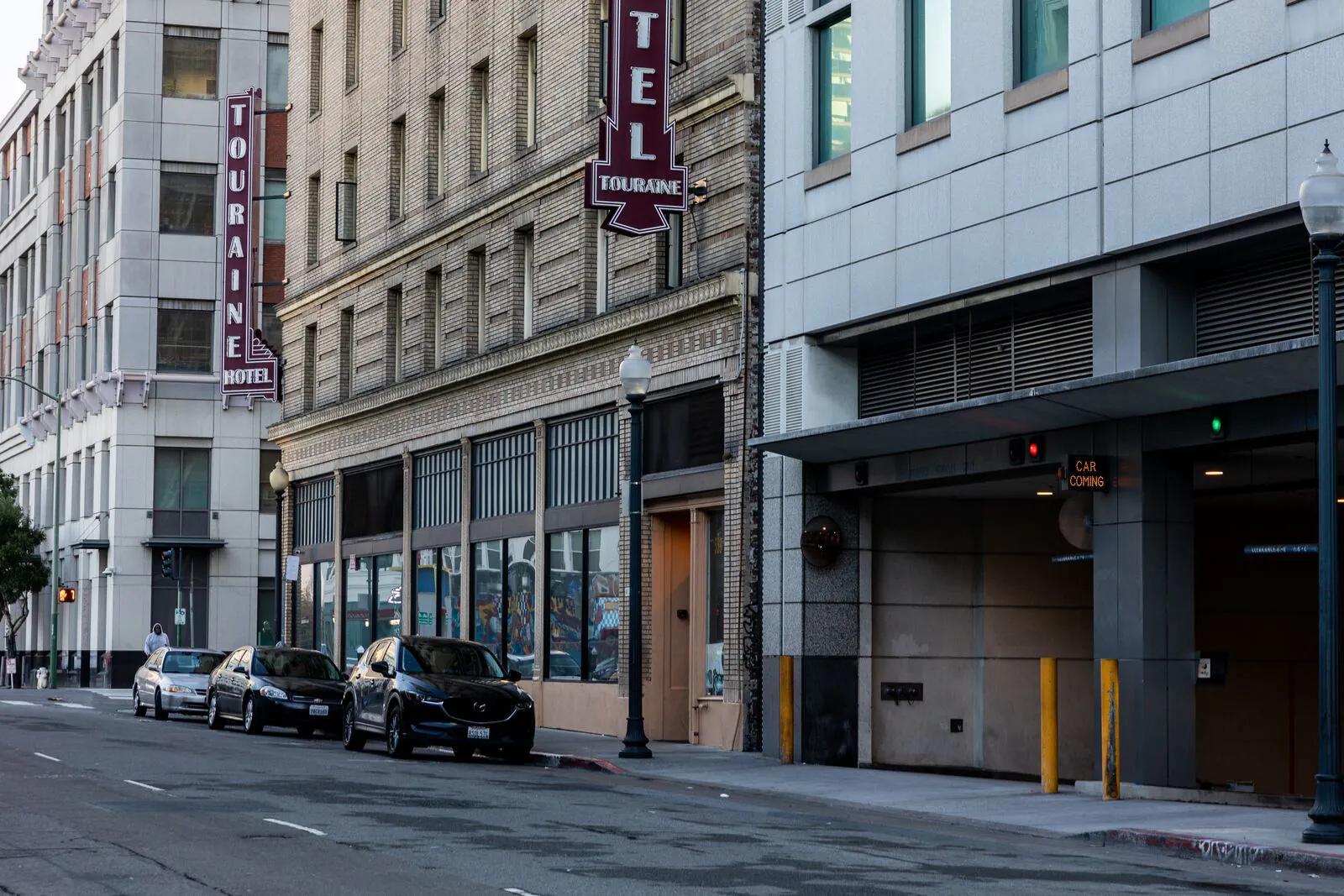 Un vieux bâtiment en brique avec des panneaux indiquant "Hôtel Touraine," à côté d'un parking dans une rue urbaine.