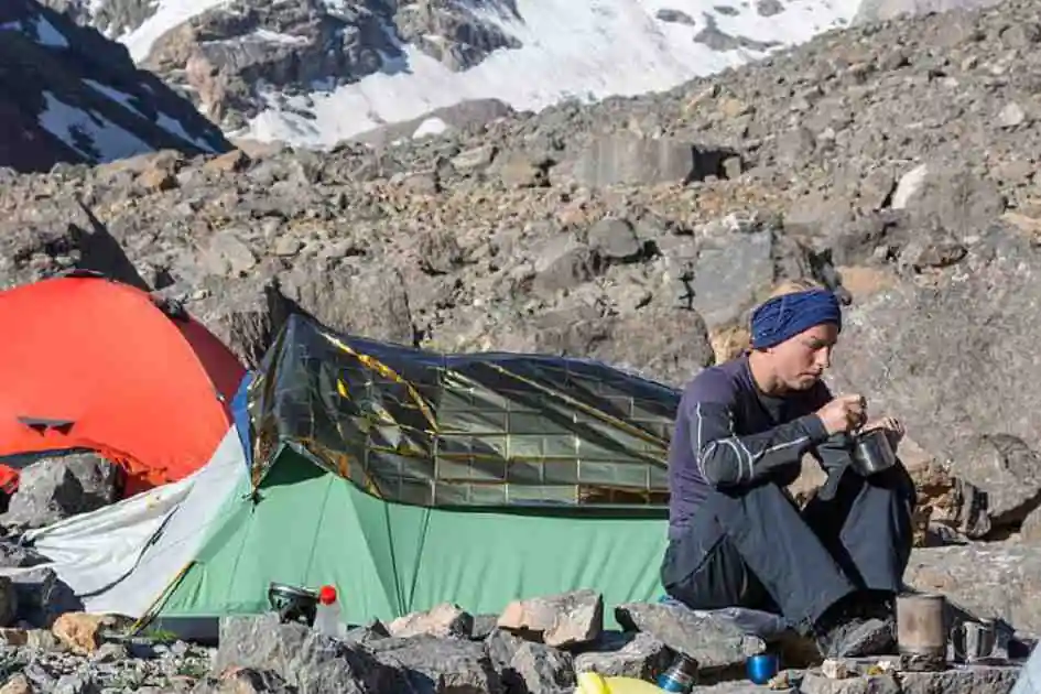 Camping-car assis à côté d'une tente et d'un sac de bivouac dans un terrain de montagne rocheuse, soulignant les différences entre un sac de bivouac et une tente.