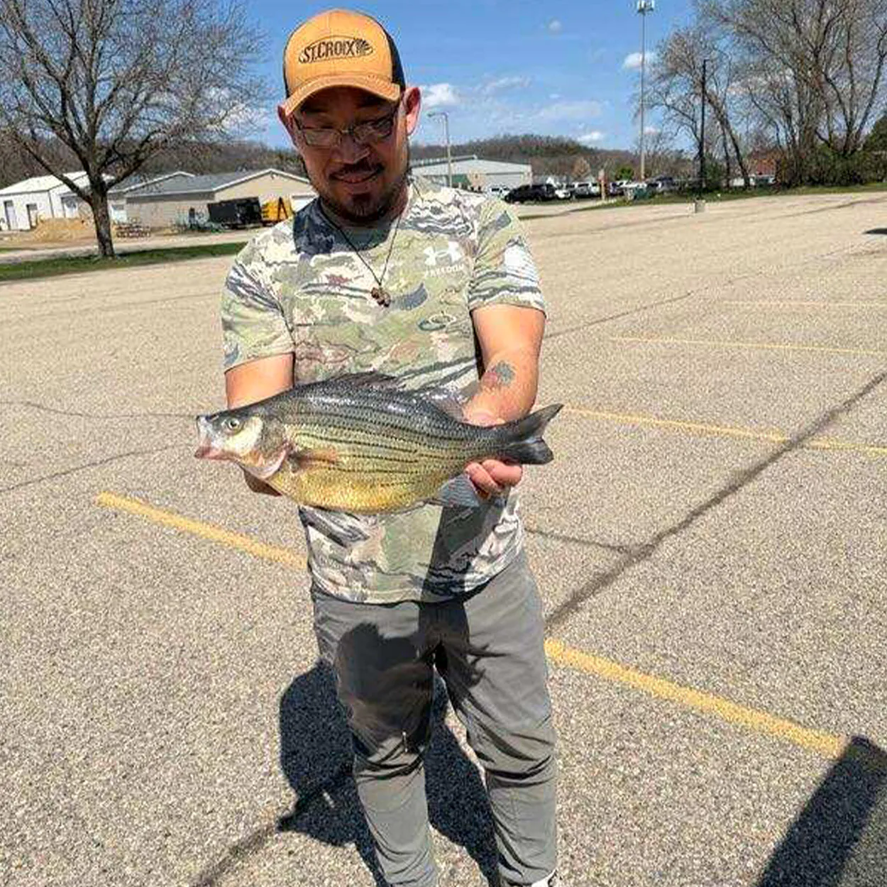 Un pêcheur tient une basse jaune dans un parking.