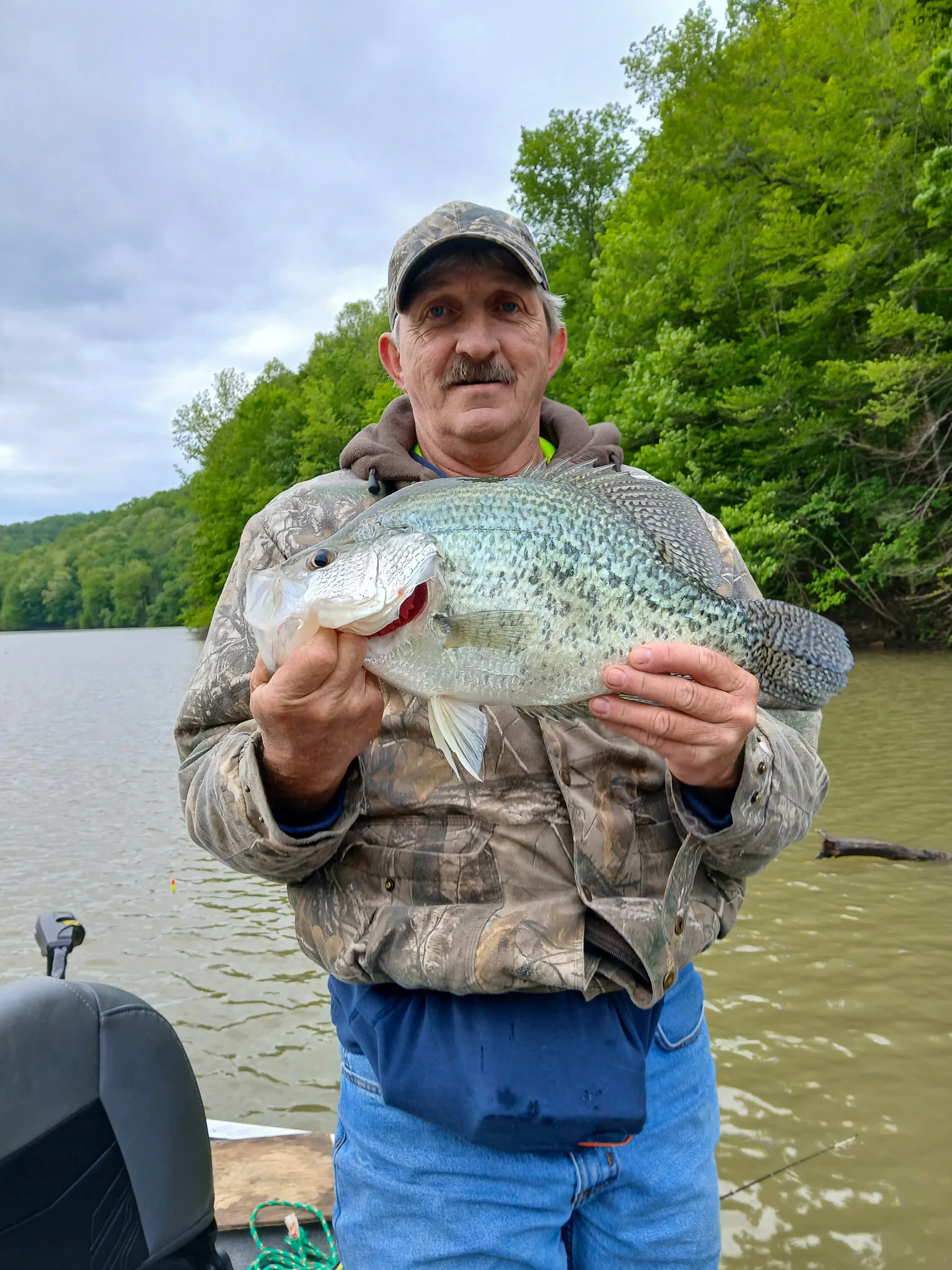 Un homme se tient sur un bateau tenant un crappie noir