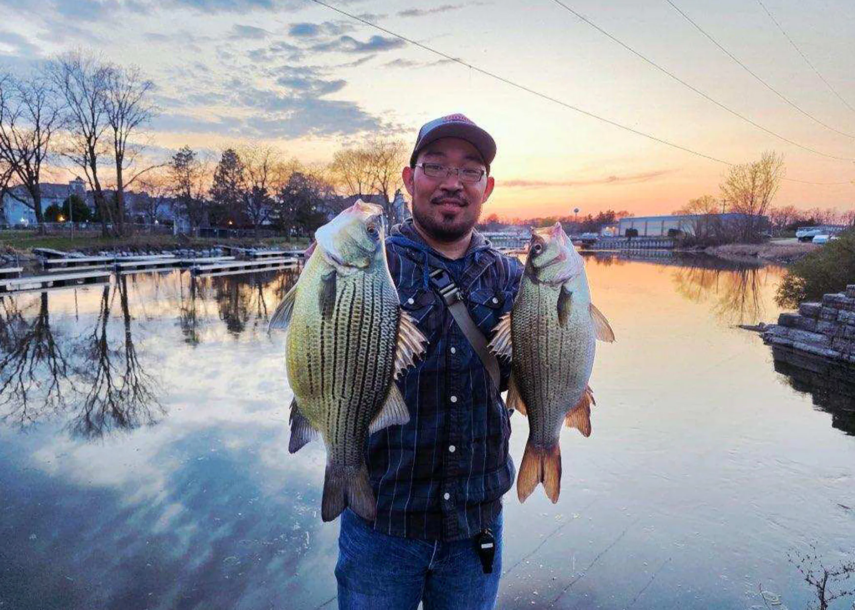 Un pêcheur maintient une grosse basse jaune aux côtés d'un bar blanc gardien.