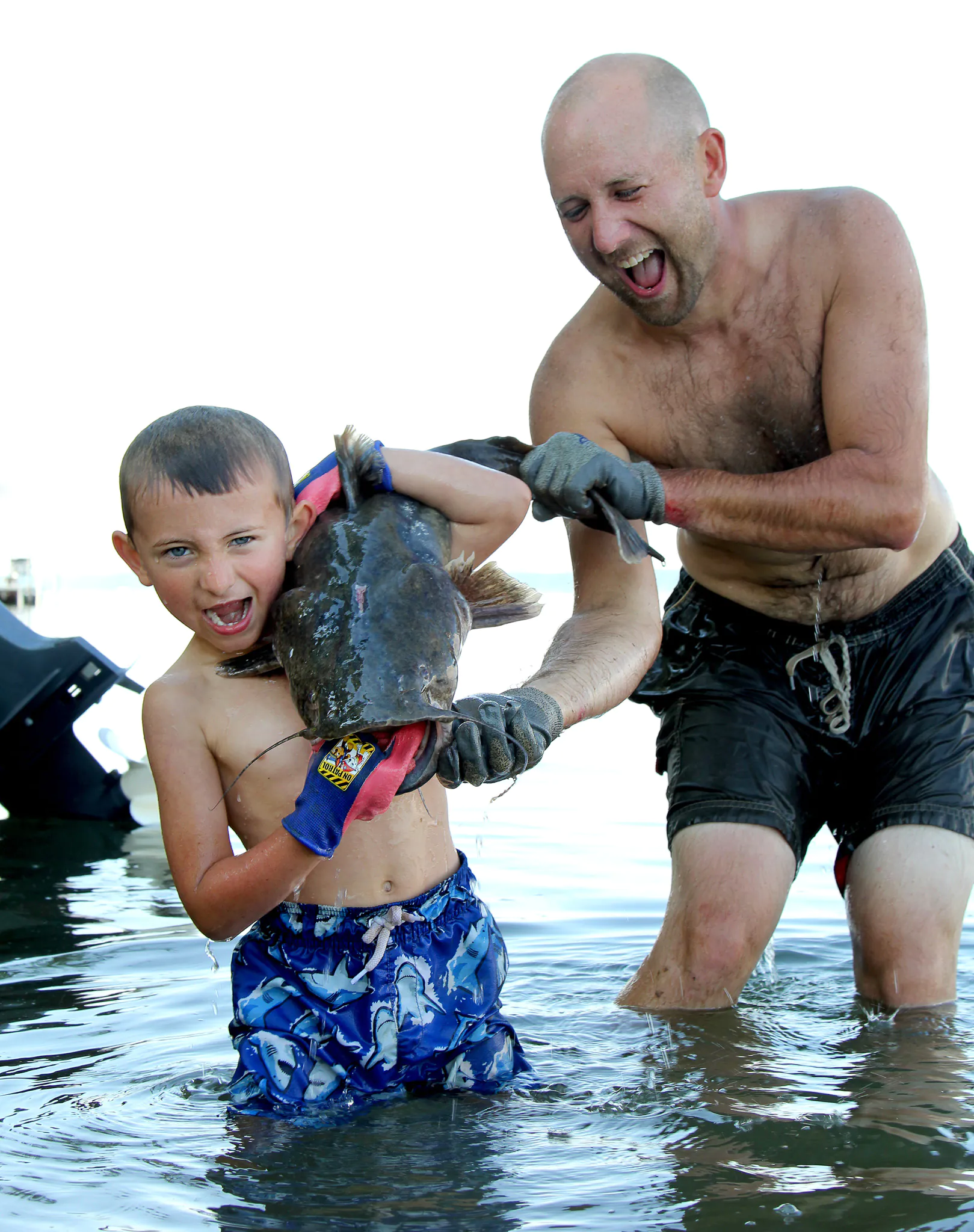 Un père aide son fils à tenir un poisson-chat à tête plate, il a écouté.