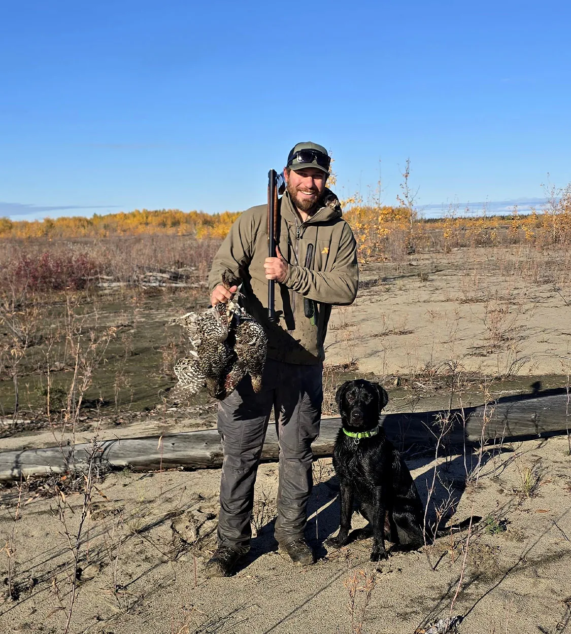 Un chasseur tient quelques tétras à côté de son chien d'oiseau.