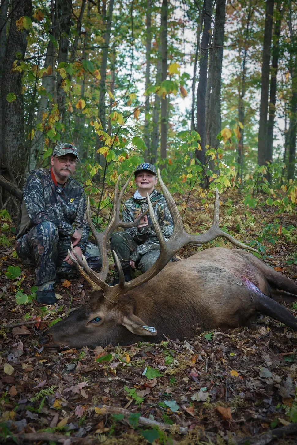 Une photo d'une fille et de son père assis derrière un gros wapiti de Pennsylvanie.