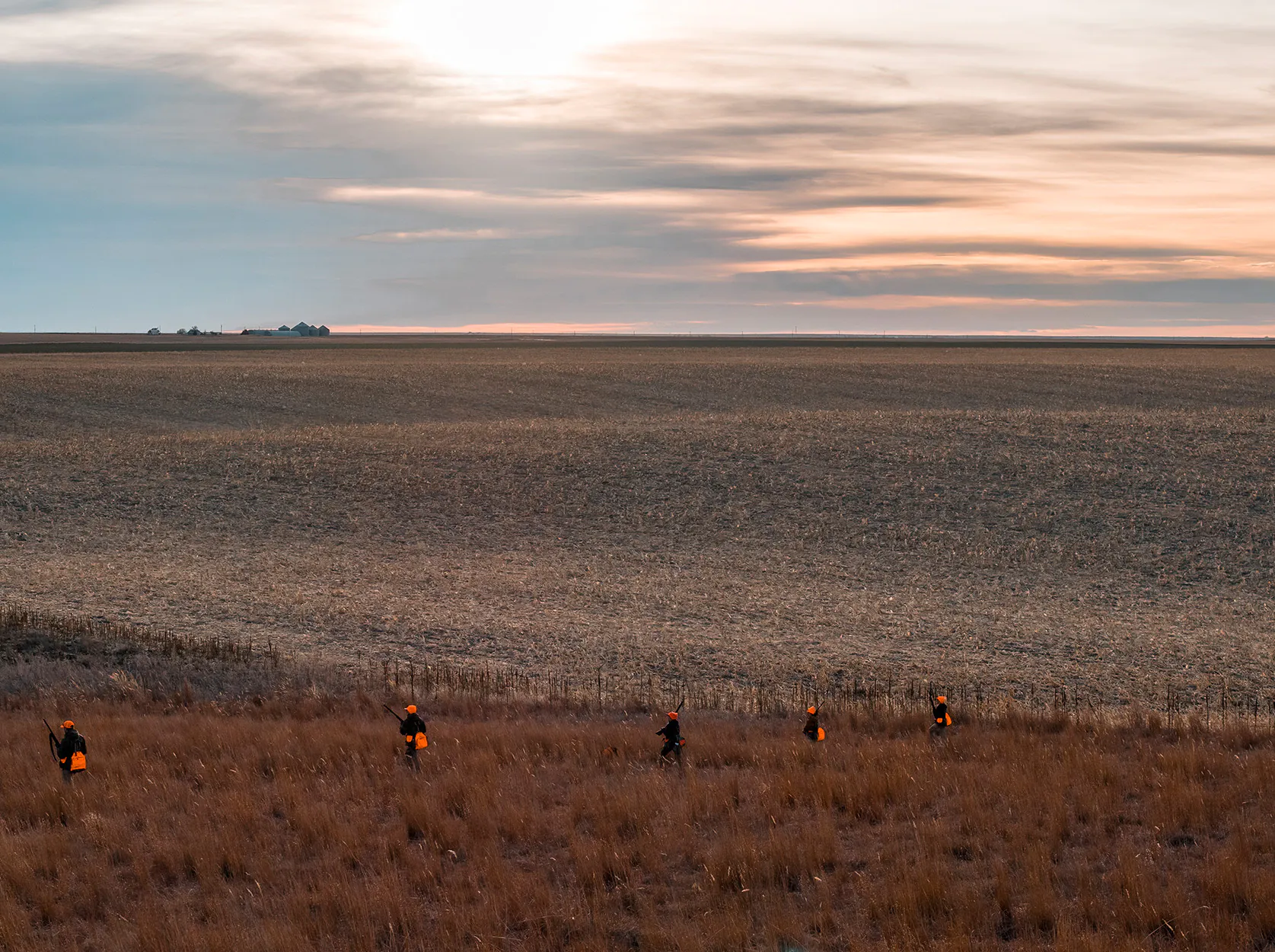 Les chasseurs traversent une vaste prairie au coucher du soleil.