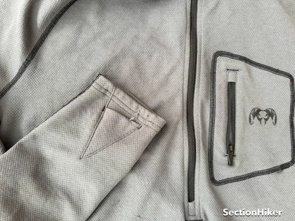 Le pull est doté d'une poche poitrine zippée et de passants pour les pouces sur les manches :