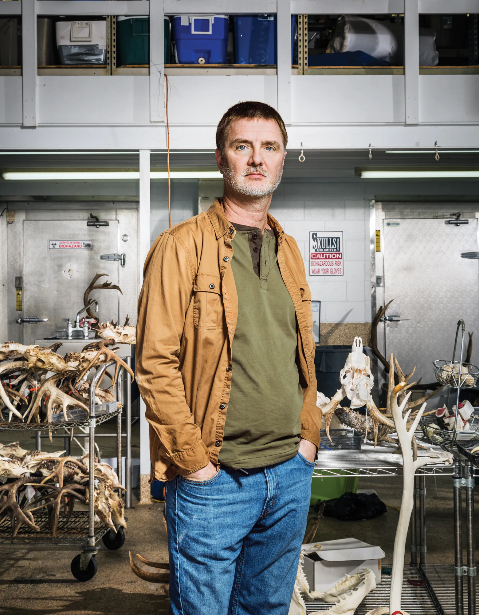 Un homme se tient les mains dans les poches devant les tables de travail d’un atelier de taxidermie.