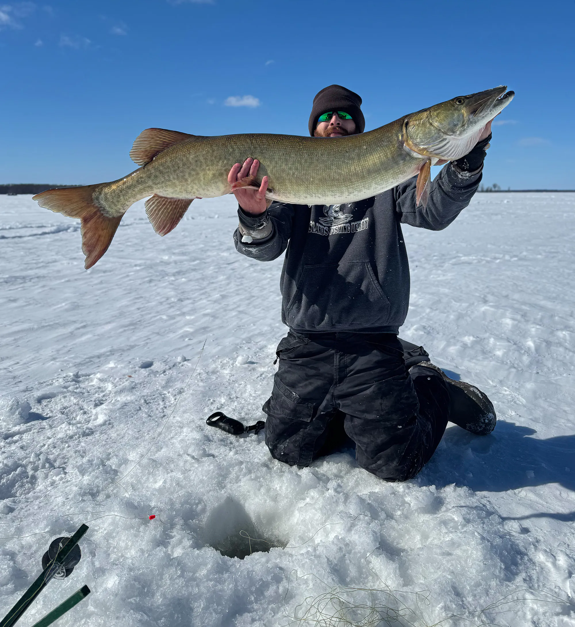 Un pêcheur à la ligne brandit un énorme Muskie du Vermont capturé à travers la glace.