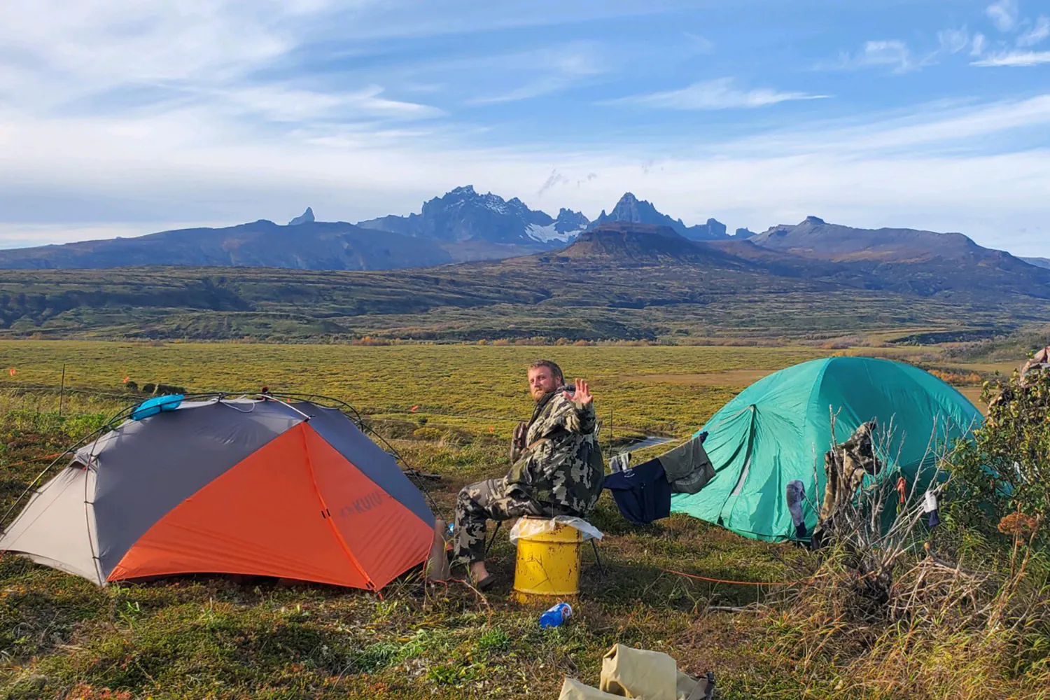 le chasseur est assis sur la toundra, entre deux tentes avec des montagnes au loin