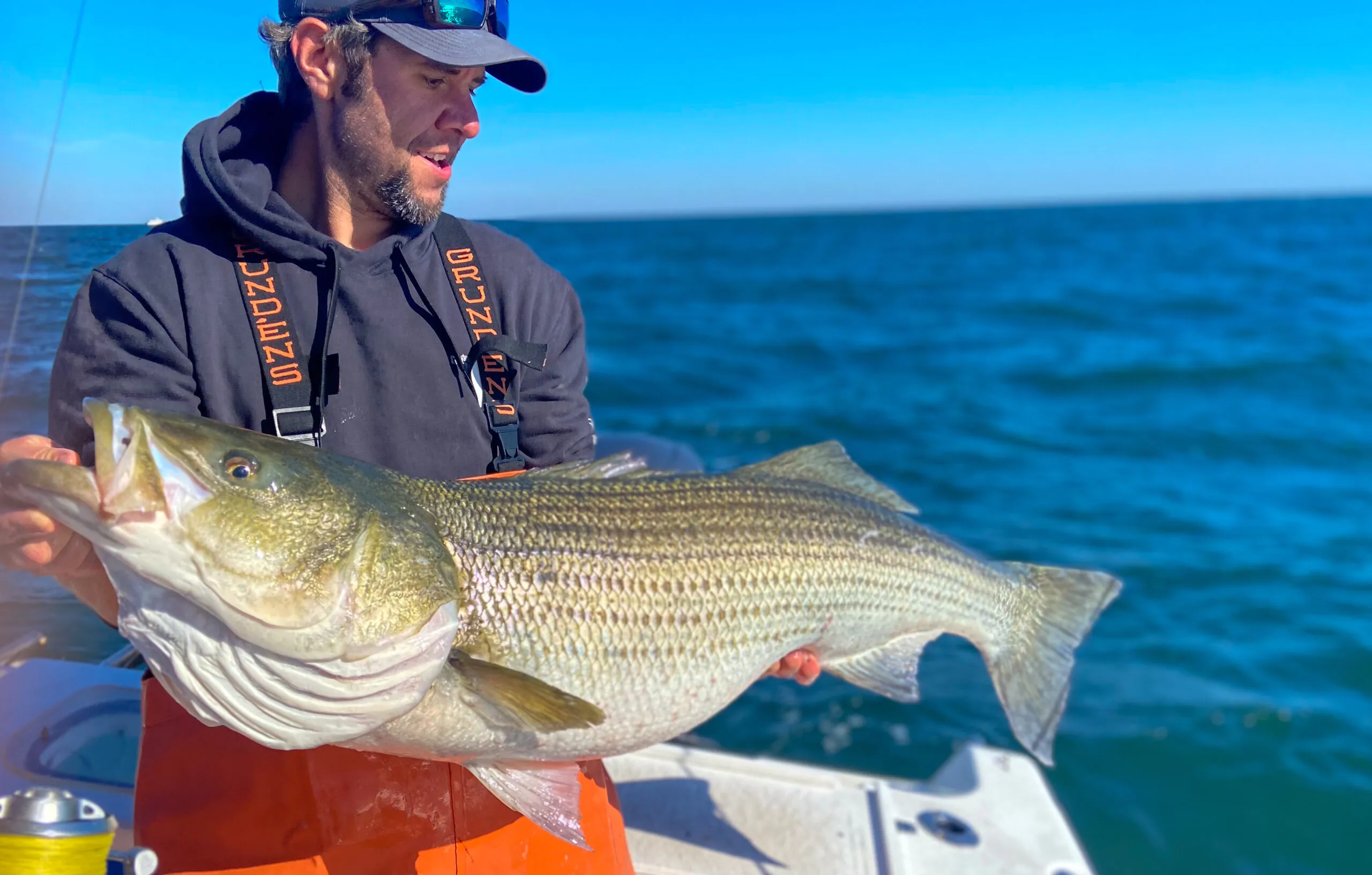 Joe Cermele avec un gros bar rayé debout sur un bateau.
