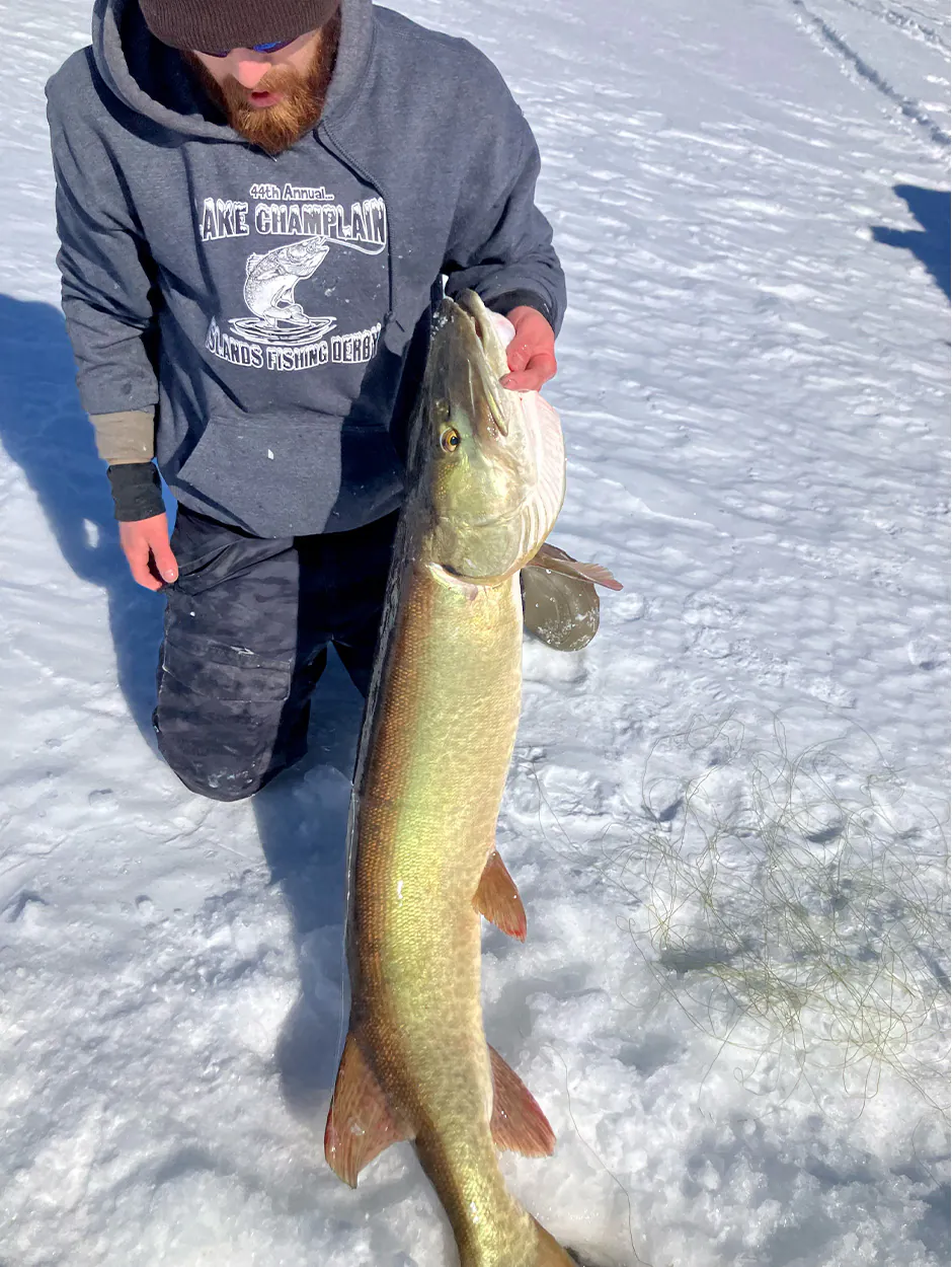Un pêcheur sur glace brandit un maskinongé sur la glace.