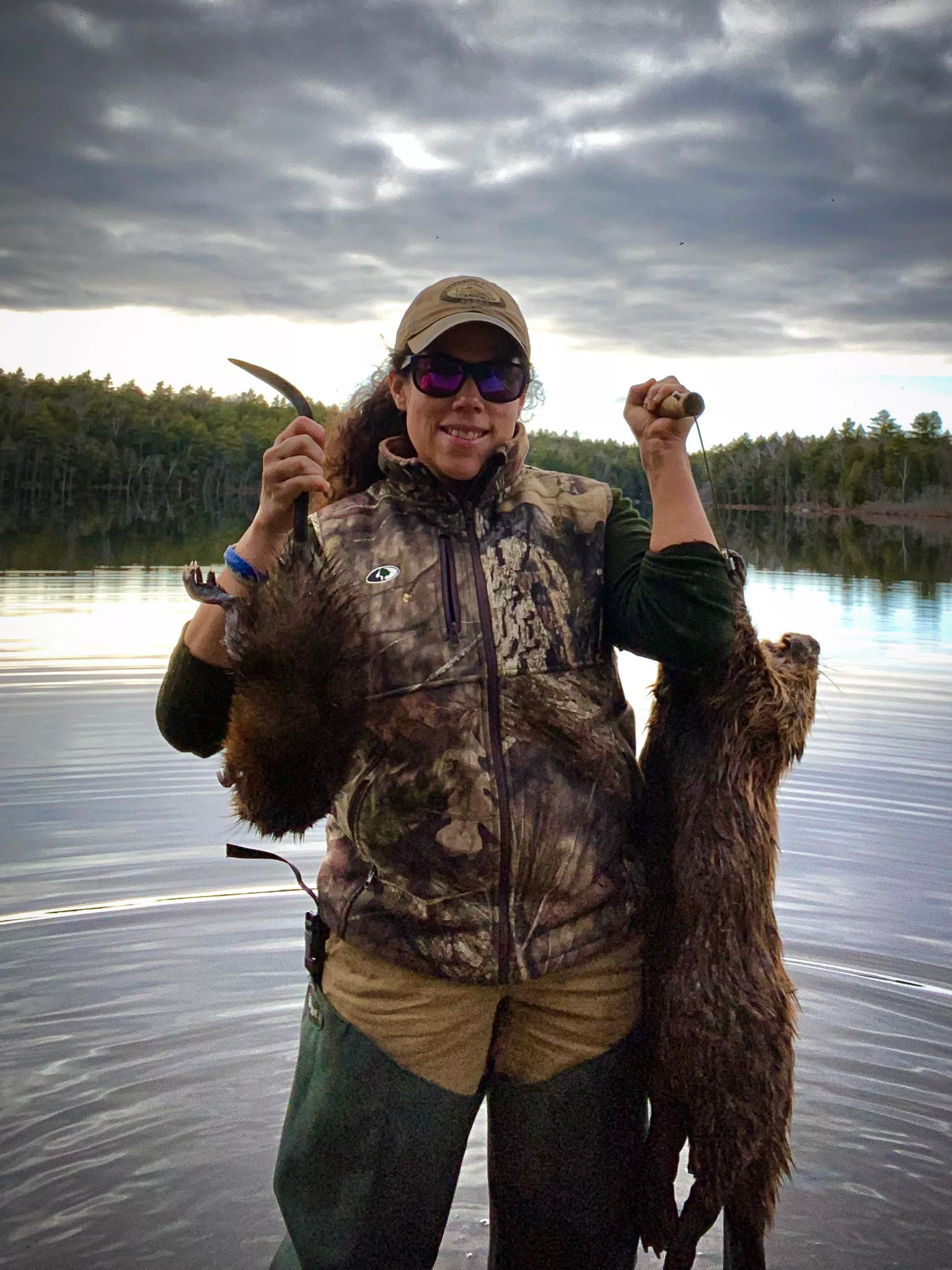 Une femme en camouflage brandit un rat musqué capturé dans la nature et un castor.